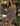 A woman stands in a sunny backyard patio setting wearing a black and white gingham tiered mini dress, holding a wine glass and carrying a black handbag.
